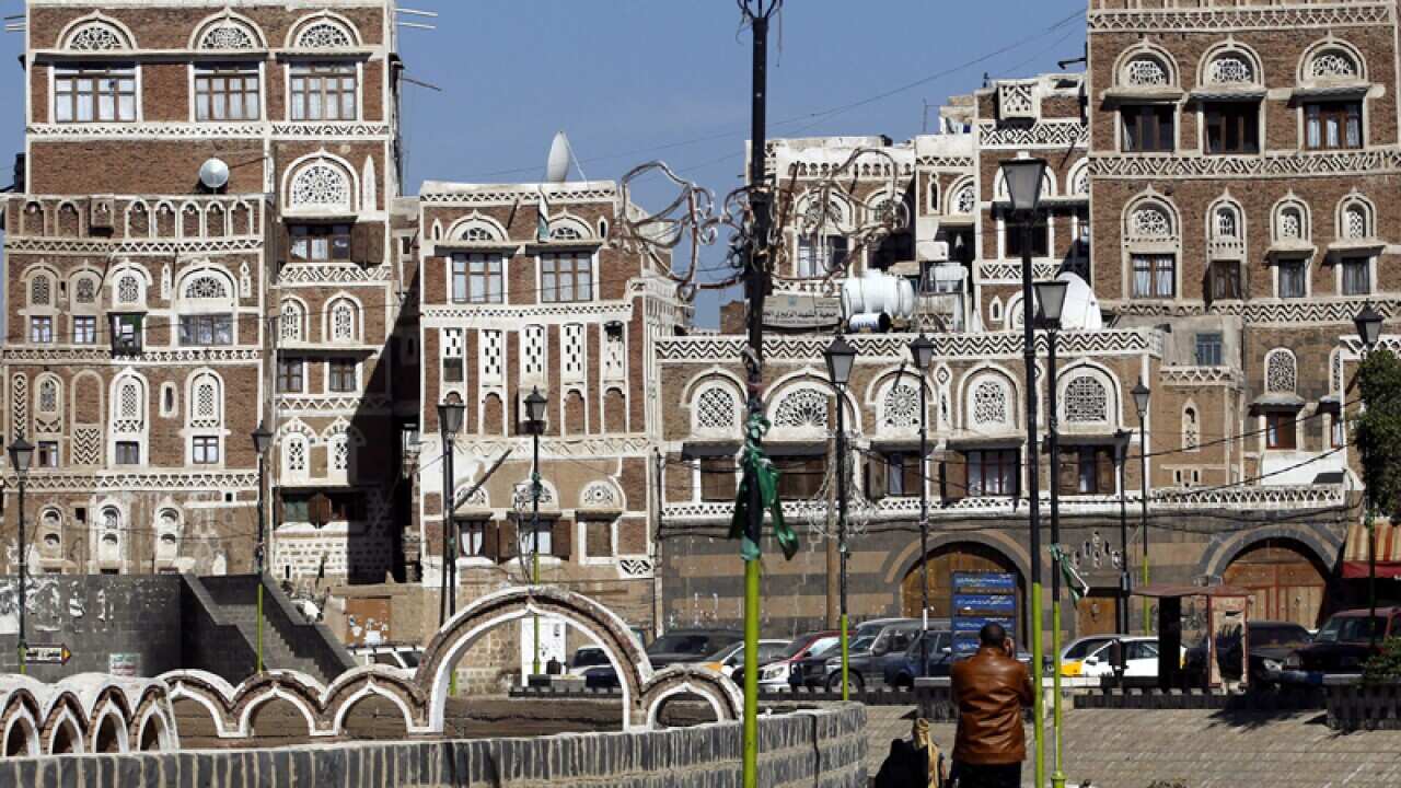 Yemenis walk in front of historic buildings in the old city of Sana’a