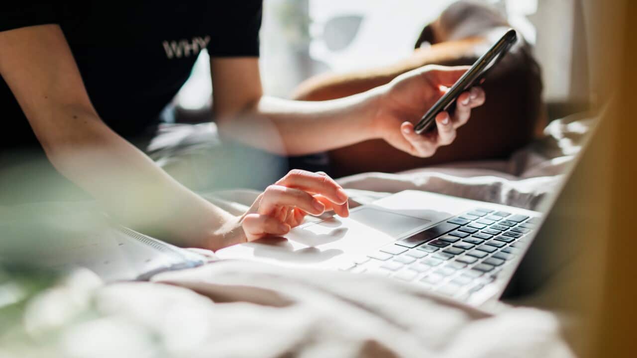 A close up of hands in front of a laptop screen holding a mobile phone
