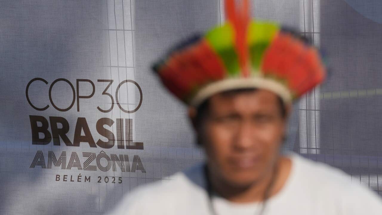 A blurred image of a man in Indigenous headwear in front of a sign that reads COP30 Brasil Amazonia