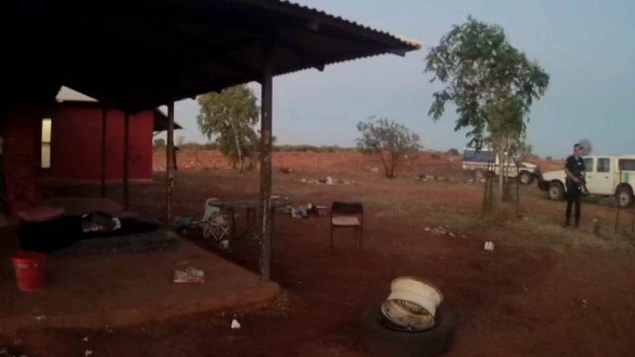 A police officer holds an AR15 assault rifle standing outside a house in the remote community of yuendumu