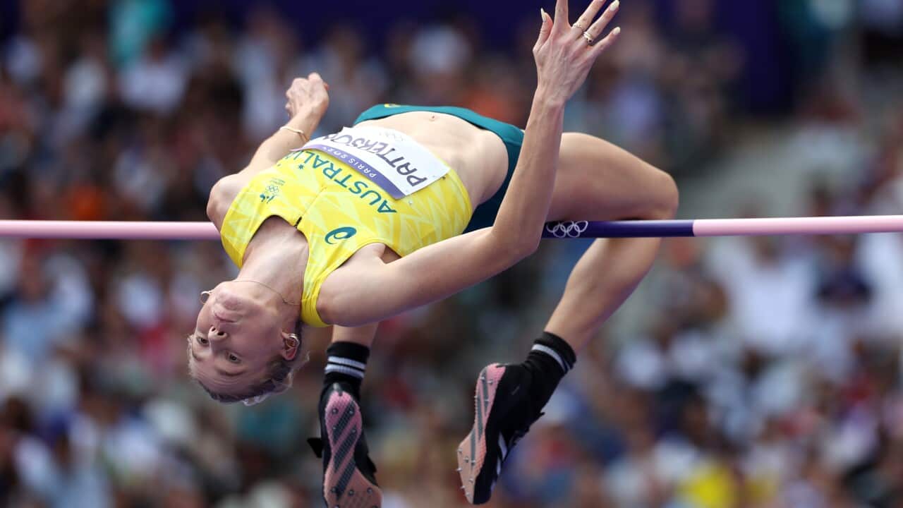 A woman jumps over a high jump bar in an Australian uniform