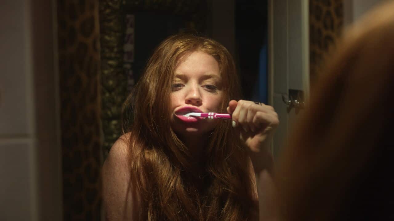 woman brushing her teeth while looking in the mirror