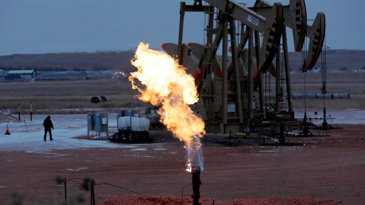 Workers tend to oil pump jacks behind a natural gas flare near Watford City, N.D.