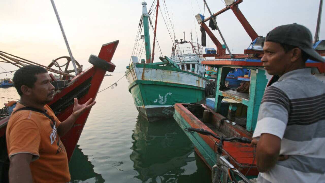 Acehnese men talk as the vessel, center, used to carry Rohingya Muslims from Myanmar and migrants from Bangladesh is docked at a port in Lhokseumawe, Aceh province, Indonesia, Thursday, May 14, 2015. (AP Photo/Binsar Bakkara)