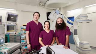 A woman and two men, wearing maroon scrubs, stand in a hospital treatment room.