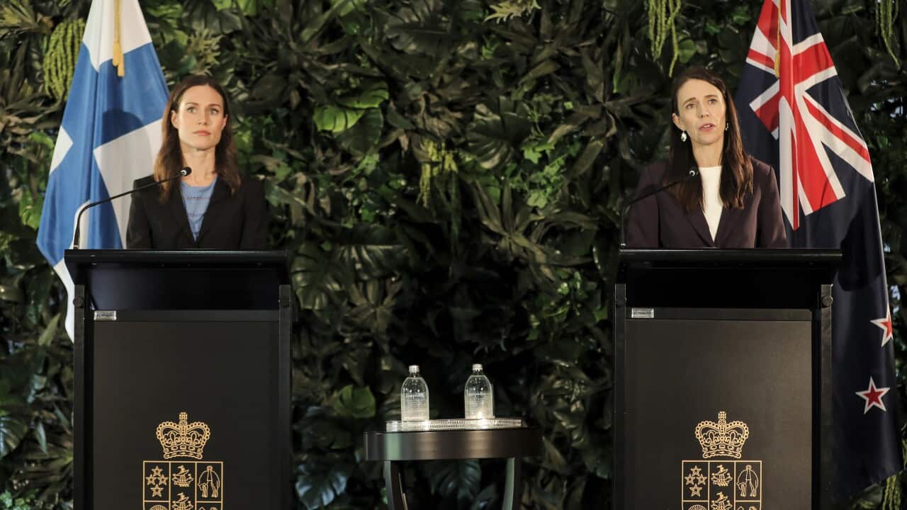 Sanna Marin (left) and Jacinda Arden (right) stand in front of their countries flags at a press conference