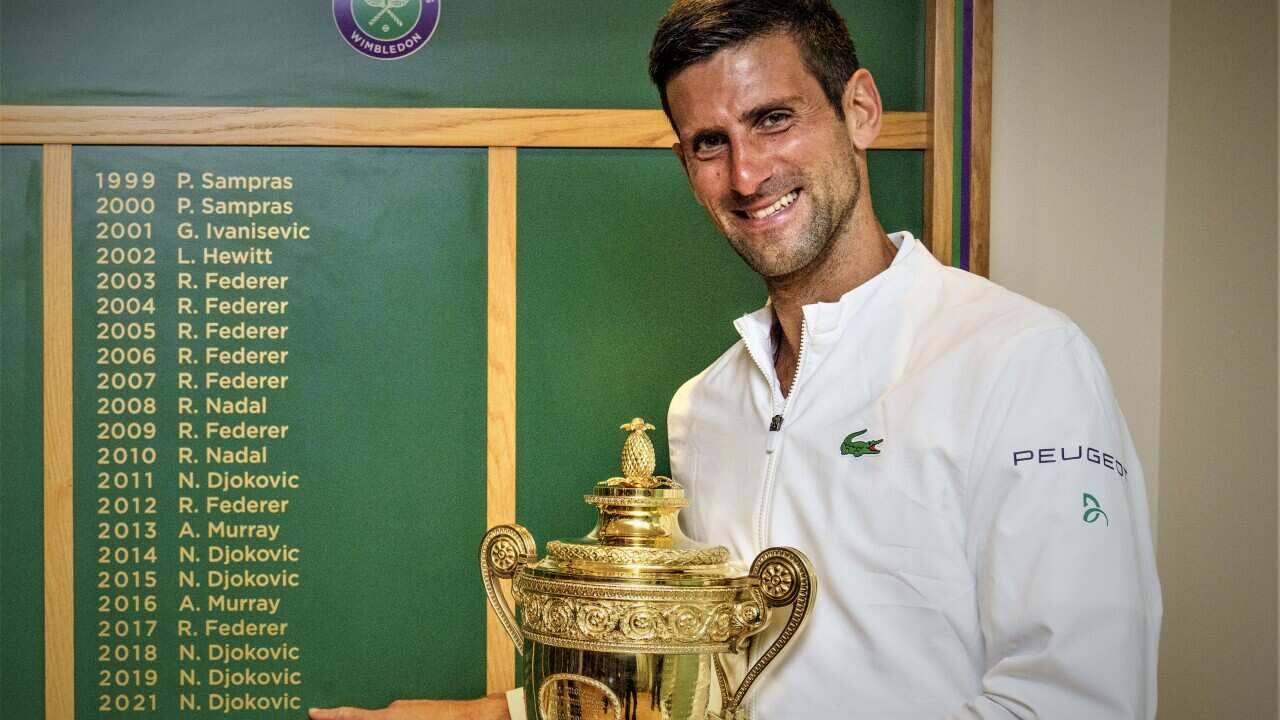 Novak Djokovic stands with the Gentlemen's Singles Trophy in front of the honours board after the mens' singles final of Wimbledon.