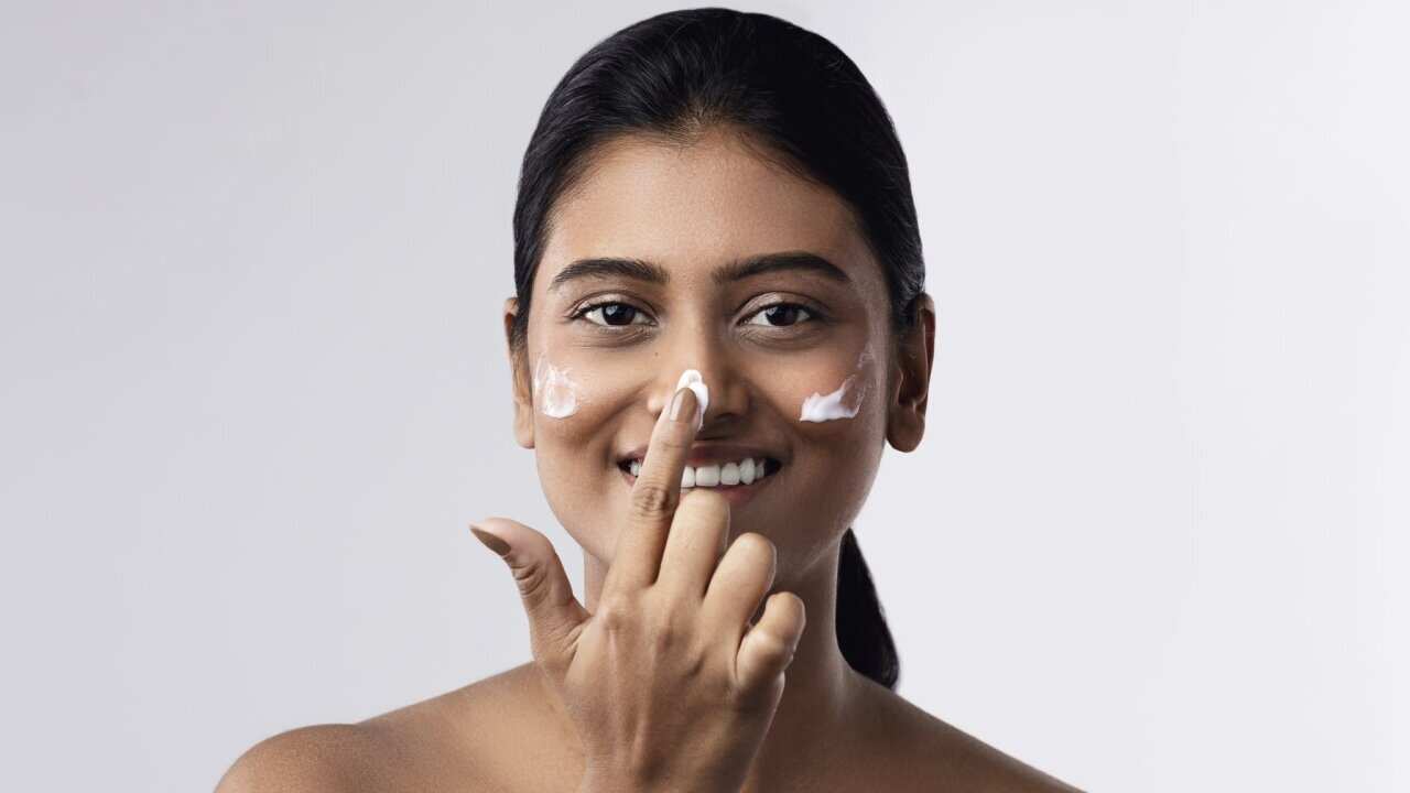 A happy Indian woman applying moisturizing cream on her face