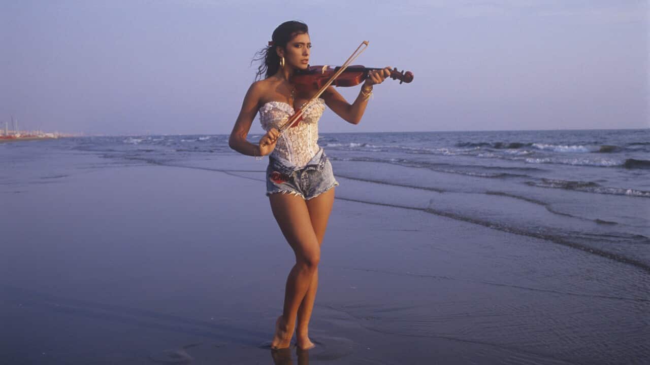 Italian-born British singer and showgirl Sabrina Salerno playing violin by the sea wearing a lace bodysuit.