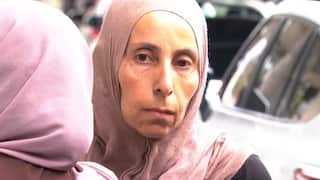 A woman wearing pink head scarf stands facing camera
