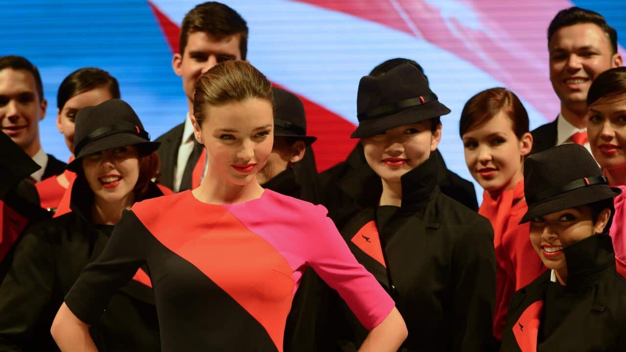 A woman in a black dress with orange and pink segments standing with her hands on her hips, in a crowd of other people in the same uniform.