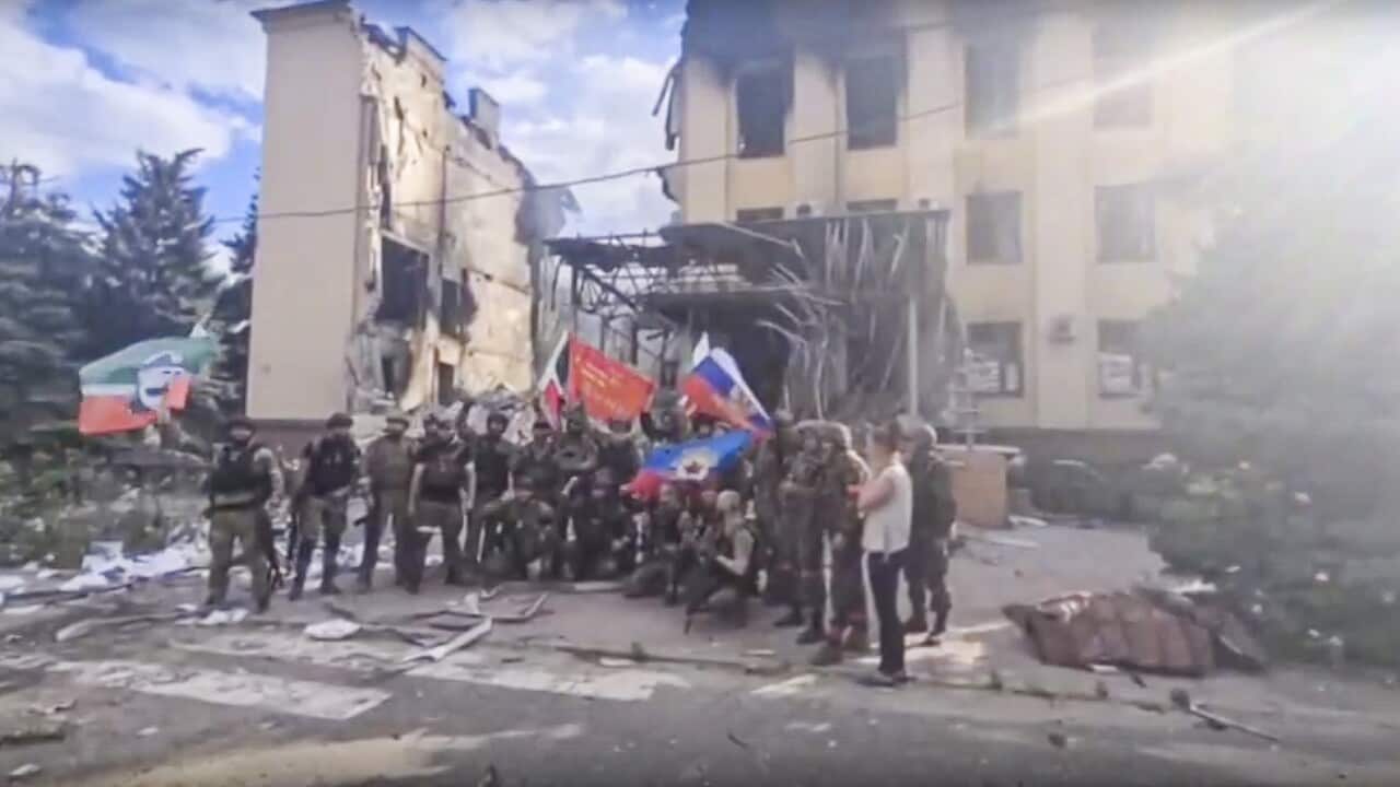 Soldiers waving Russian flag in front of destroyed building