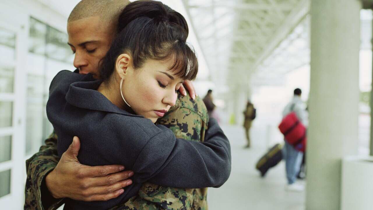 Young couple embracing in airport, man in military uniform