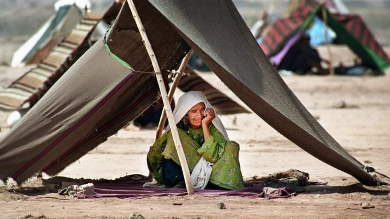 Huddled under a makeshift tent an elderly woman waits for her family to return