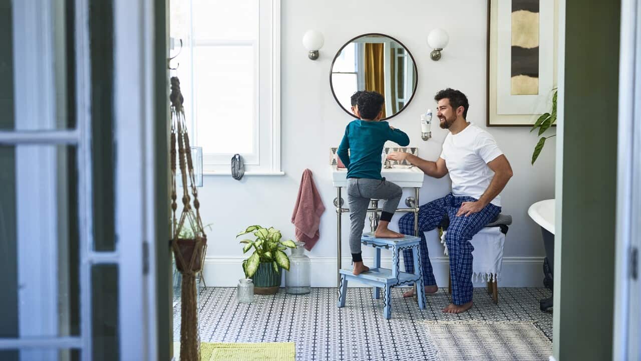 Father helping son brushing teeth in bathroom