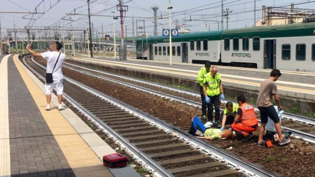 Rescue services help woman hit by train while a man takes a selfie.