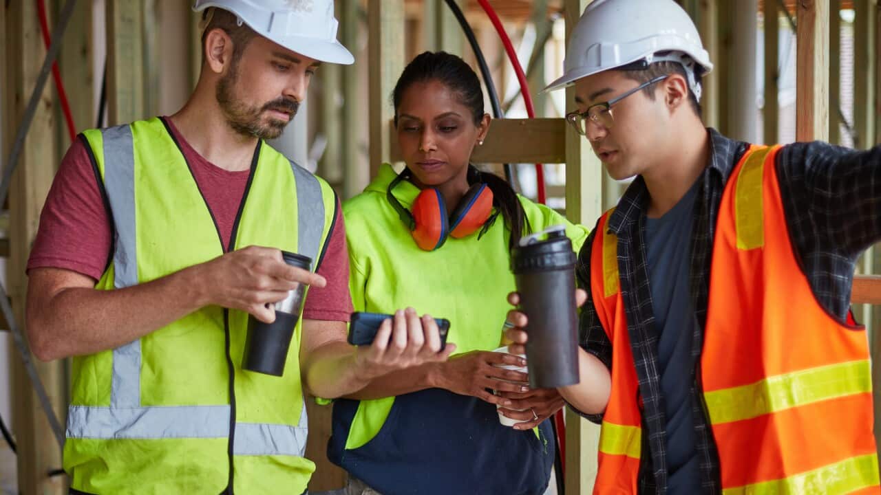 Engineer showing mobile phone to coworkers at site