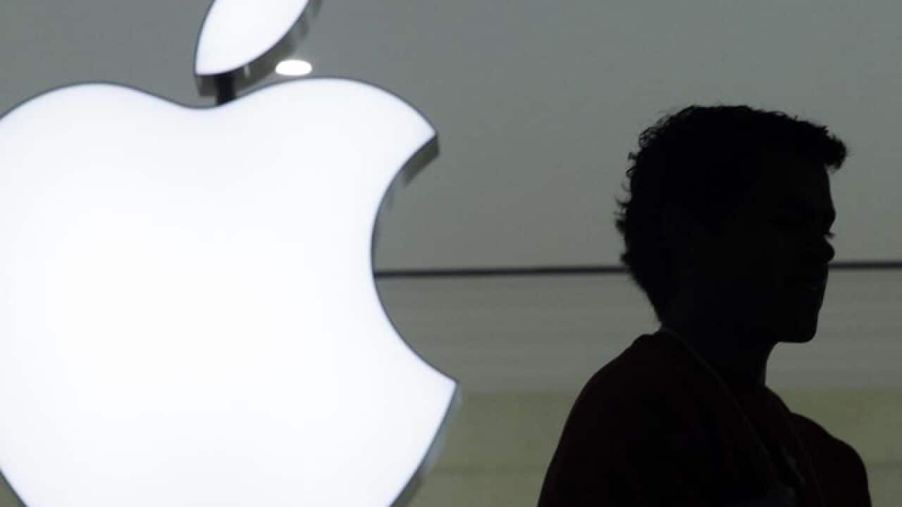person stands near the Apple logo at an Apple store.
