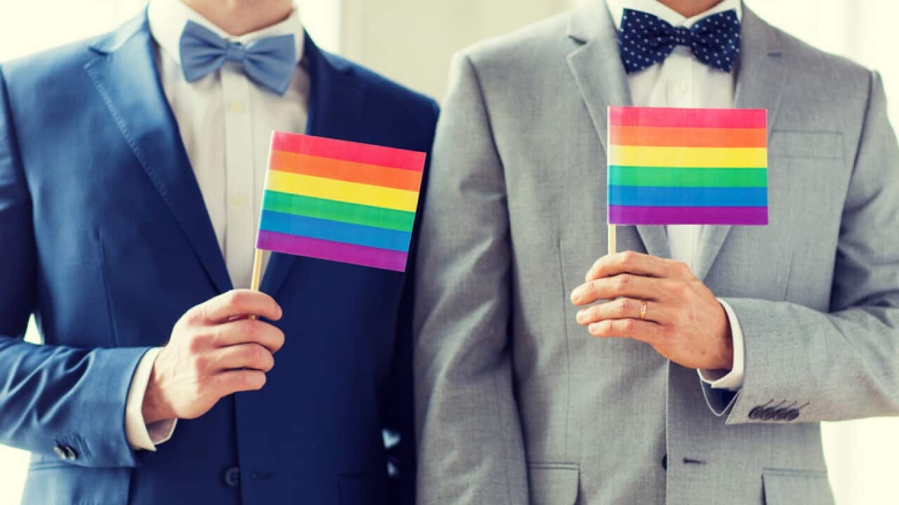 close up of male gay couple holding rainbow flags