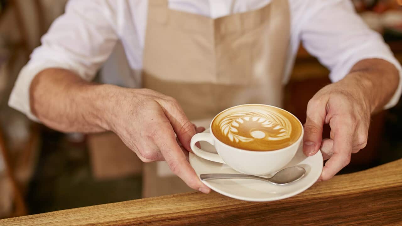 Close-up of man in apron serving coffee while standing in coffee shop. Barista giving you a cup of fresh coffee at cafe.
