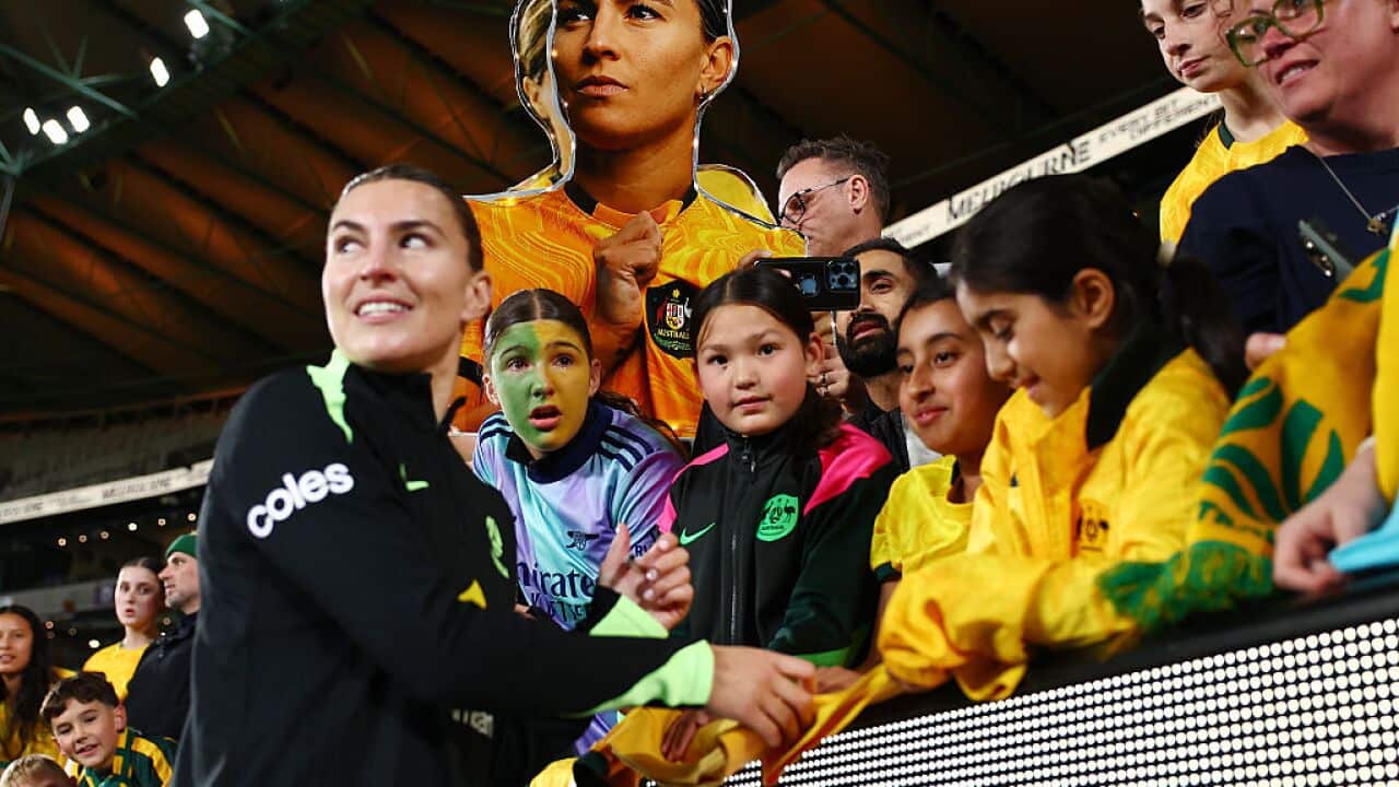 A female football player in a black jersey is meeting with her young fans in a stadium.