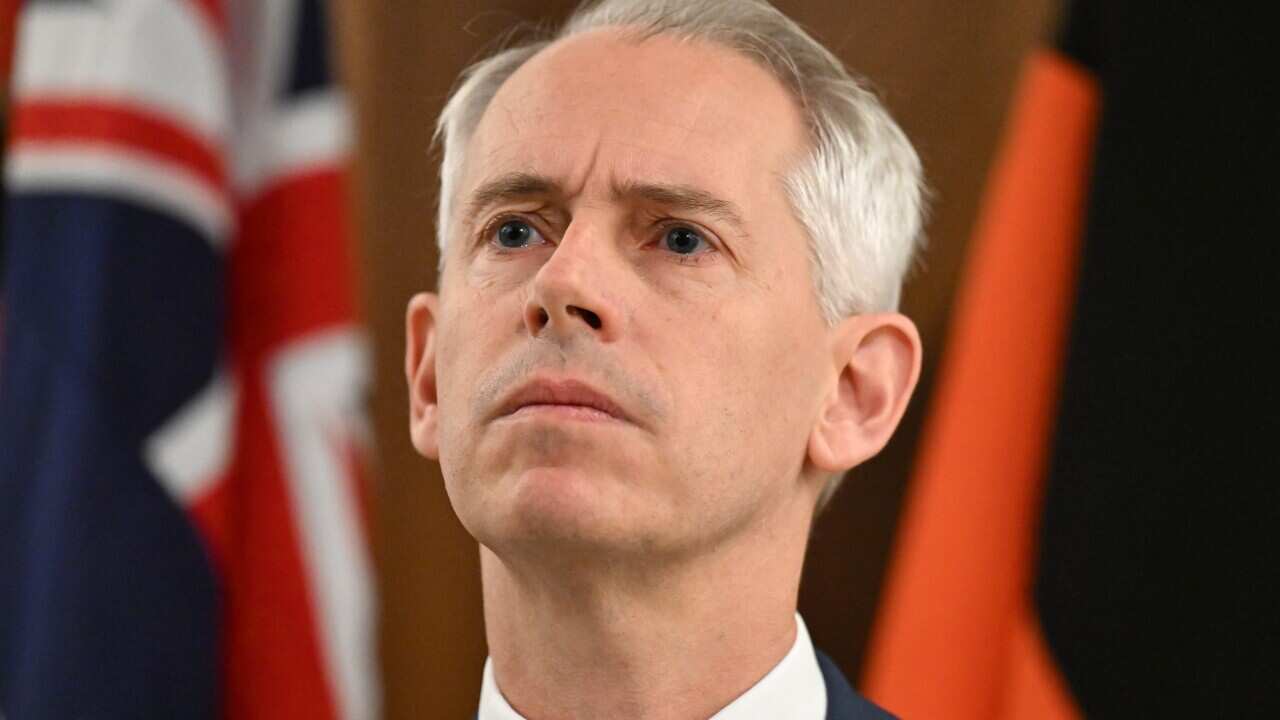 Andrew Giles standing in front of Australian and Aboriginal flags.