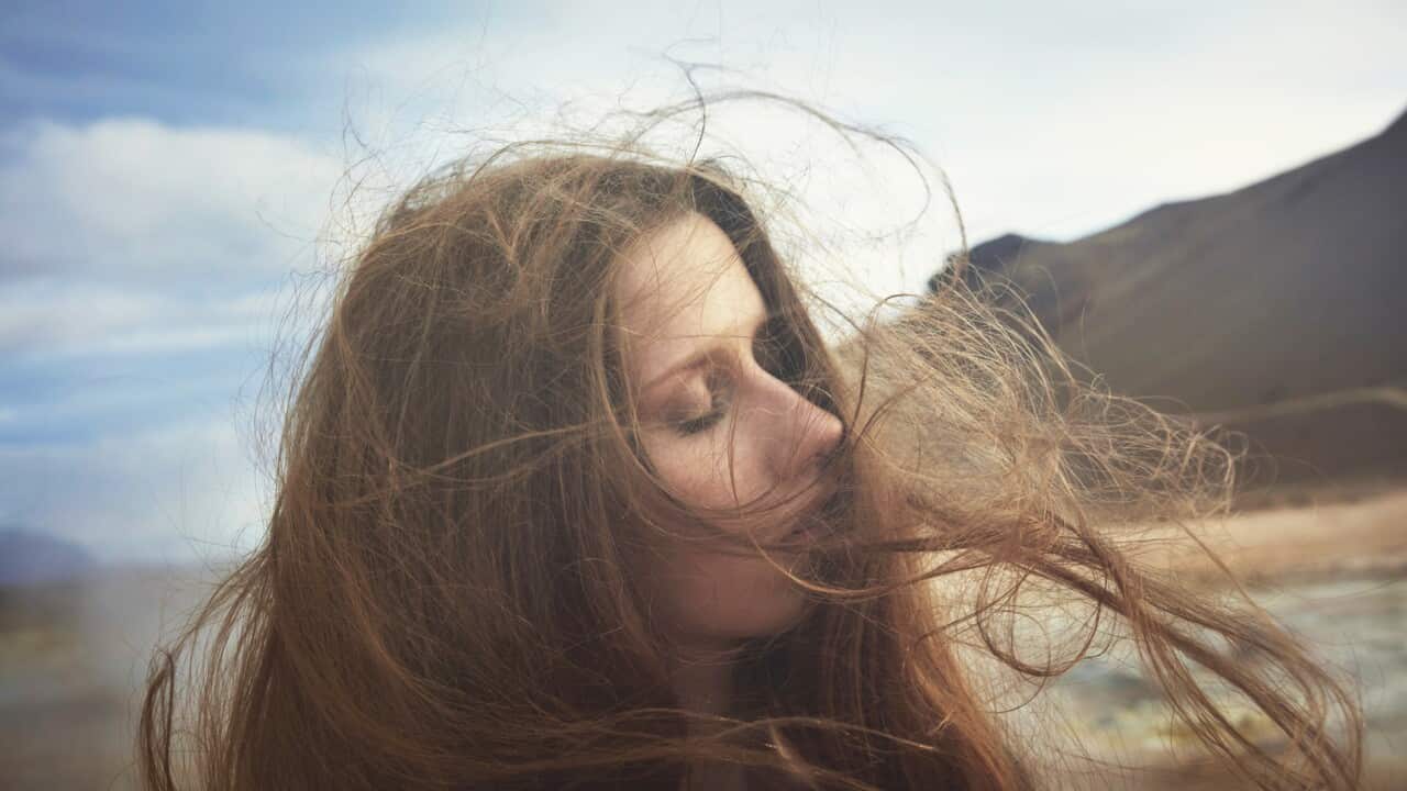 Woman standing outside, her long hair whipping around her face in the wind.