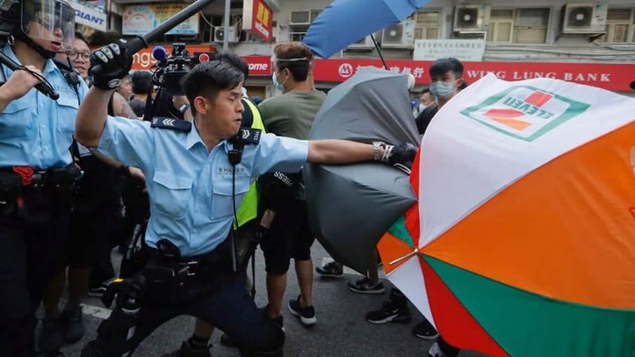A police officer attacks protesters holding up umbrellas in Hong Kong.