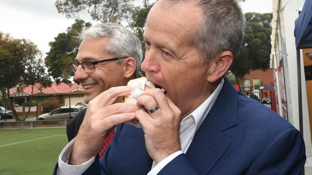 Bill Shorten bites a sausage sandwich at a Victorian polling booth.