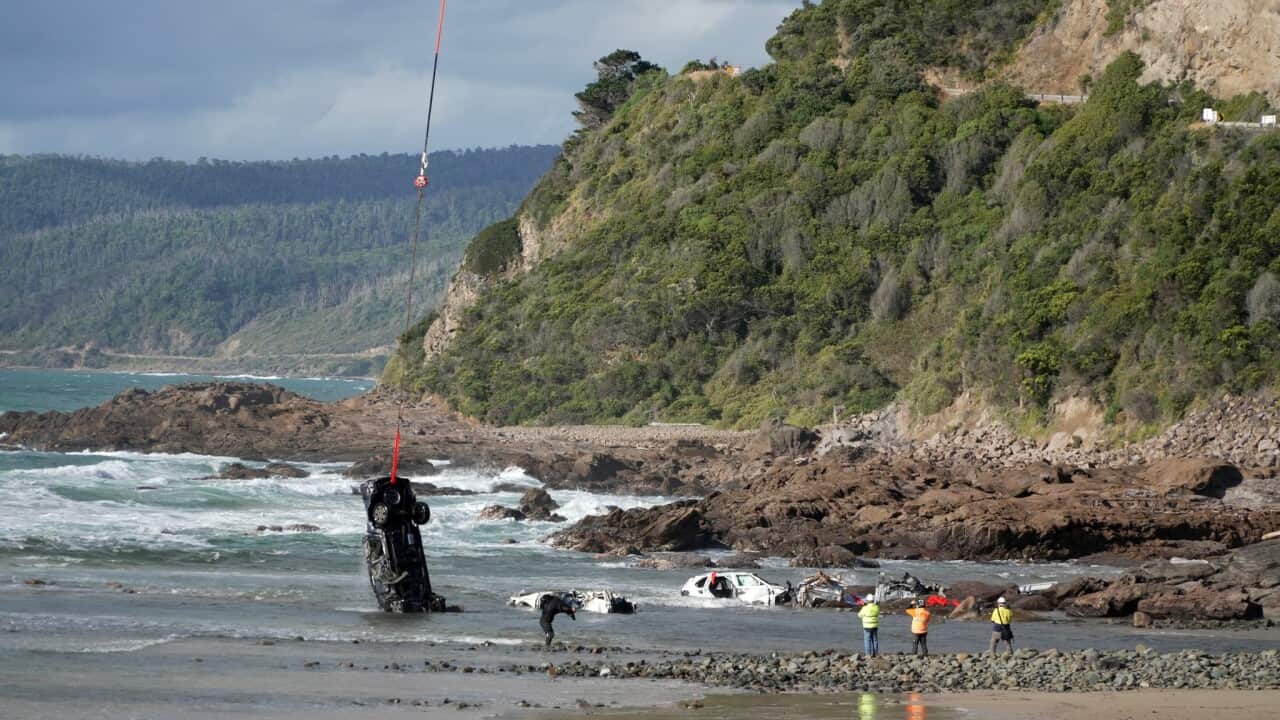 A car being winched from the ocean. The wreckage of several other cars can be seen in the water.