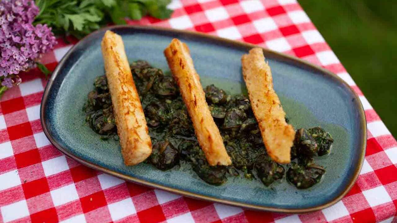 A rectangular plate sits on a red checked tablecloth. It holds a dark stewish dish, topped with three toast fingers.