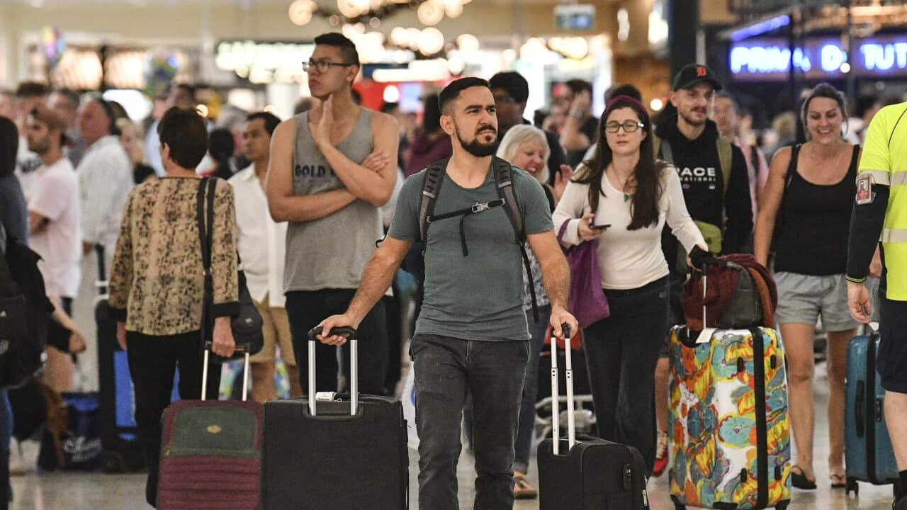 People walking through the arrivals and departures hall of an airport. Some are wheeling suitcases.