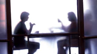 Two people's silhouettes behind a glass door. They're seated at a table talking.