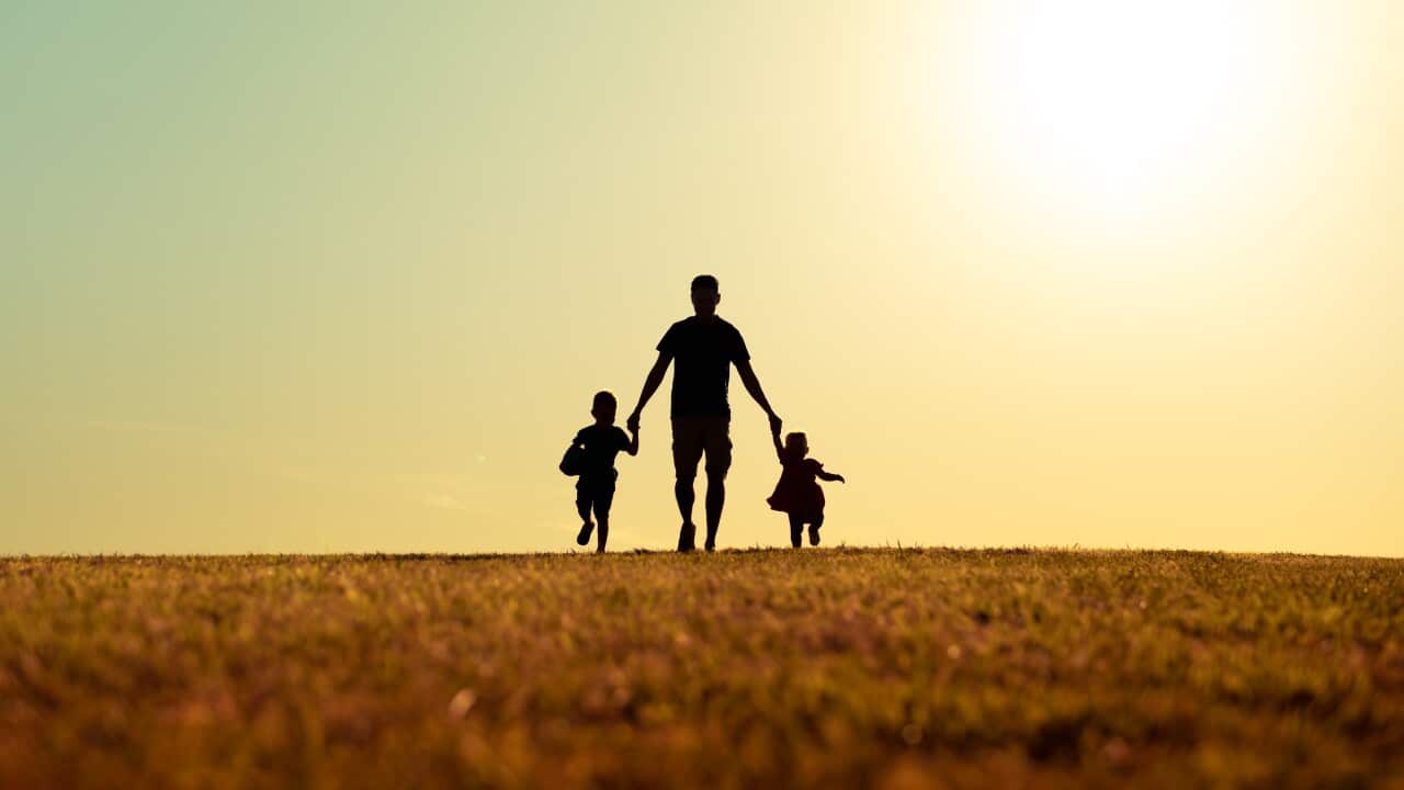 Father walking with son and daughter in park at sunset.