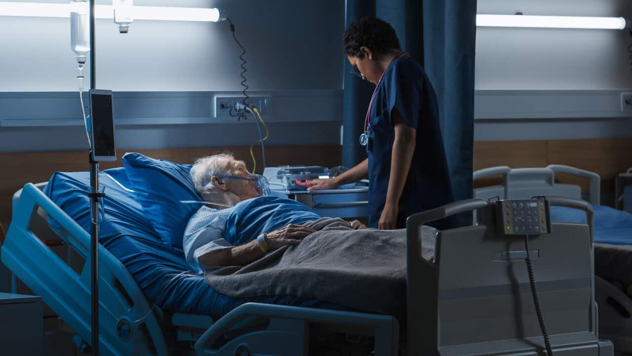 An elderly man wearing an oxygen mask in a hospital with a doctor standing beside him.