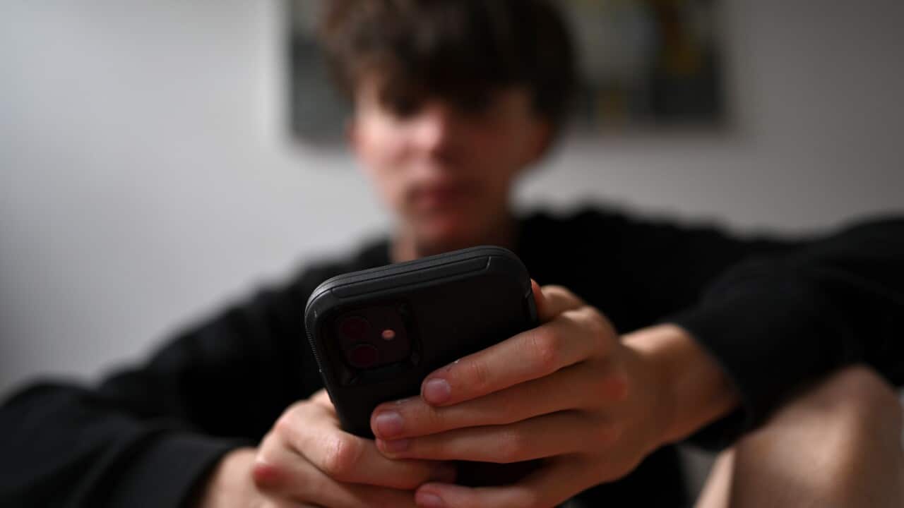 A teenager dressed in all black uses his mobile phone.