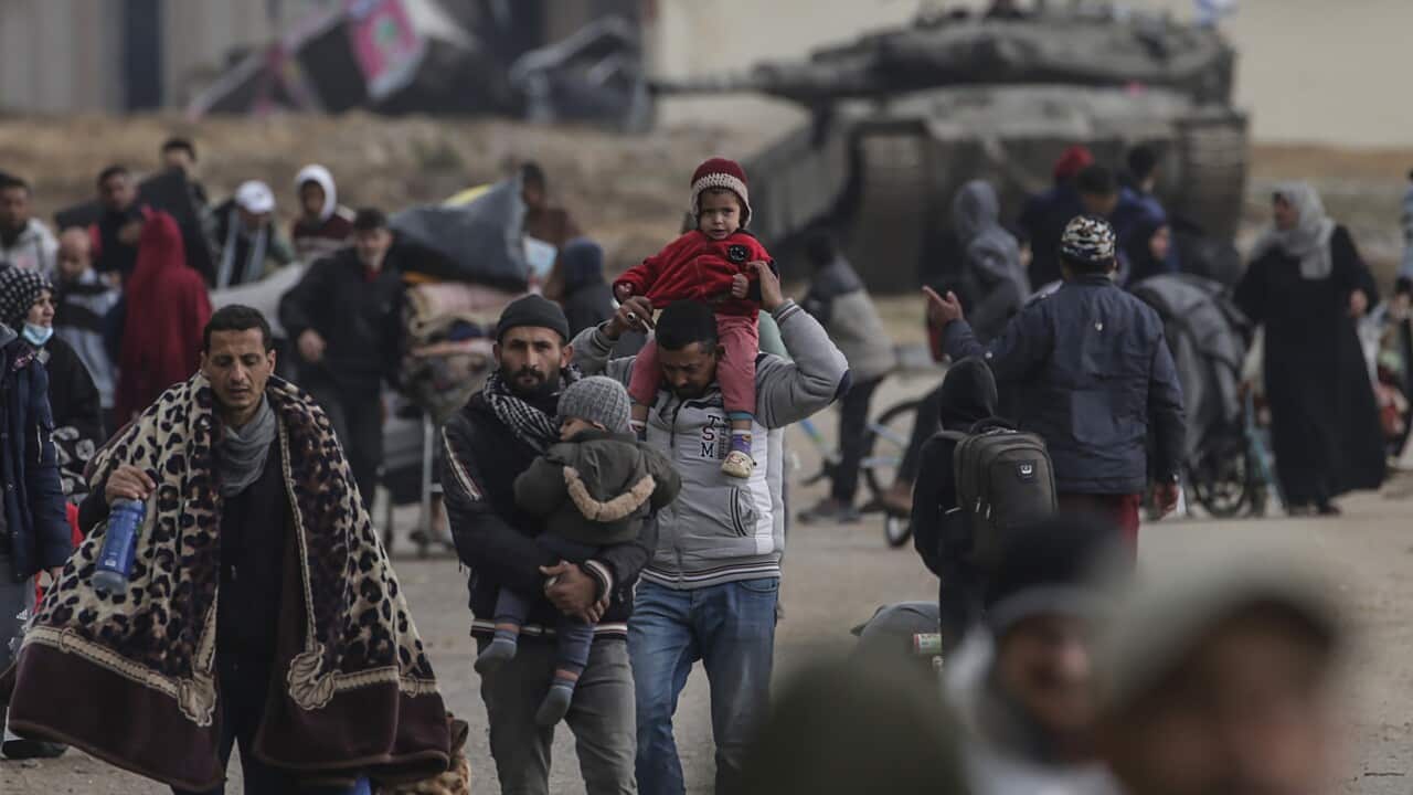 A group of displaced Palestinians move past Israeli tanks in a camp