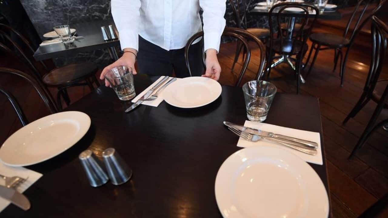 A waitress is seen setting up a table at a restaurant in Canberra