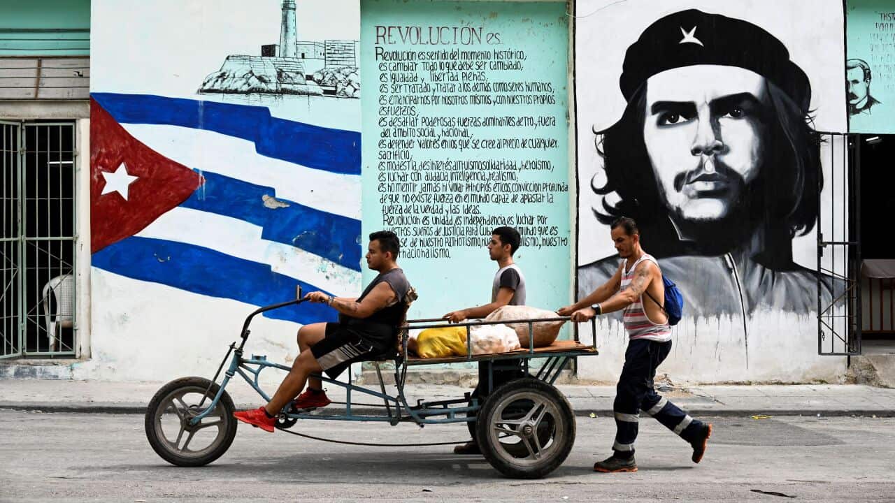 People transport food in a tricycle passing by a wall painted with the Cuban flag and a portrait of Argentine-born revolutionary leader Ernesto "Che" Guevara in a street in Havana