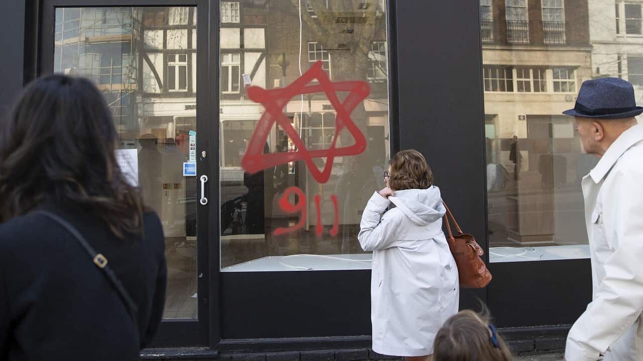 People look at anti-Semitic graffiti on a shop window in Belsize Park, North London.