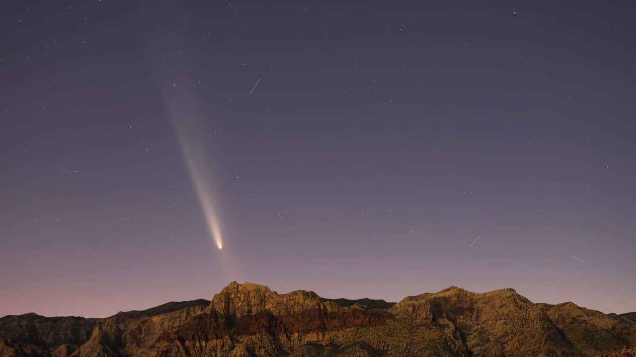 A comet streaks through a dark blue and purple sky with rugged mountains visible below.