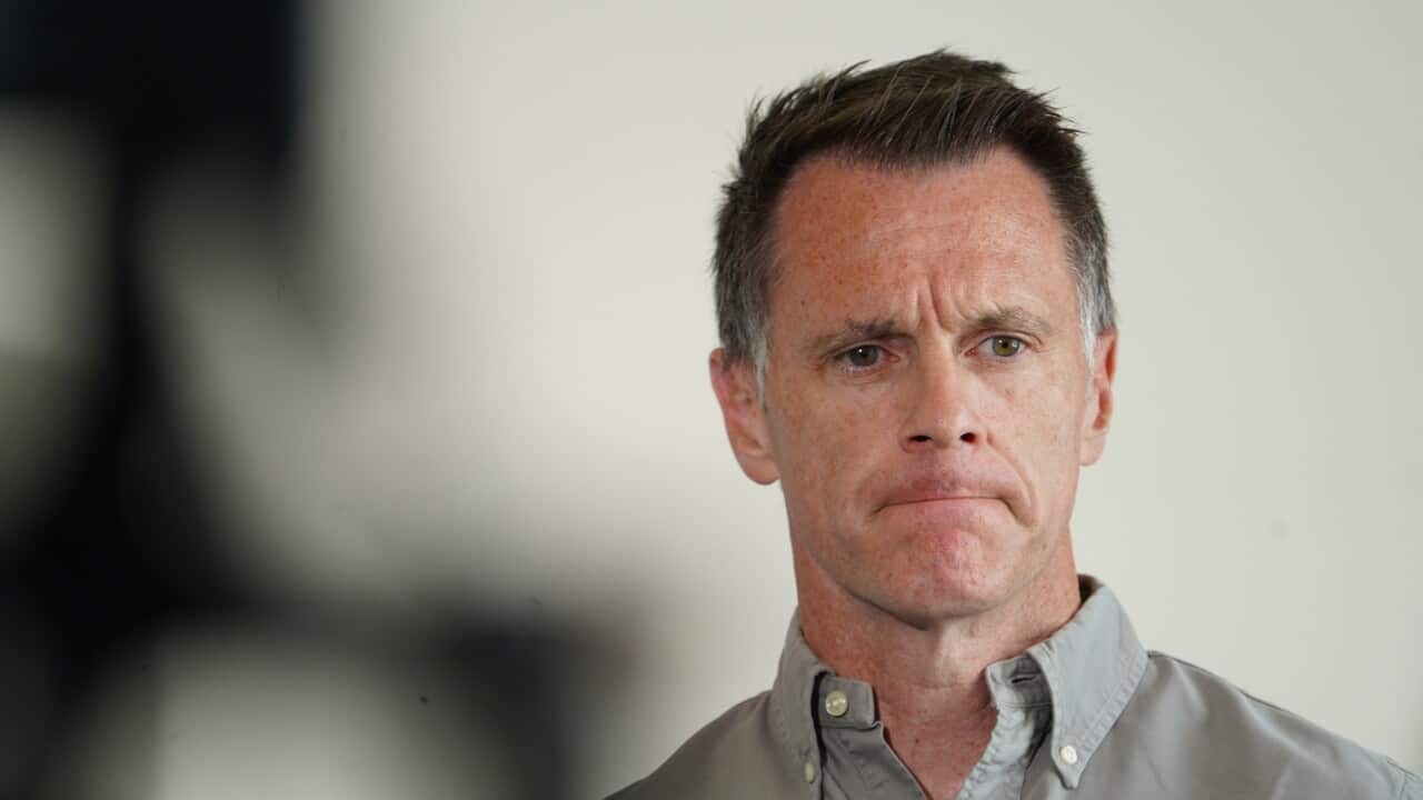 A middle-aged man with short, dark hair and a sombre expression looks slightly off-camera while wearing a grey button-down shirt.
