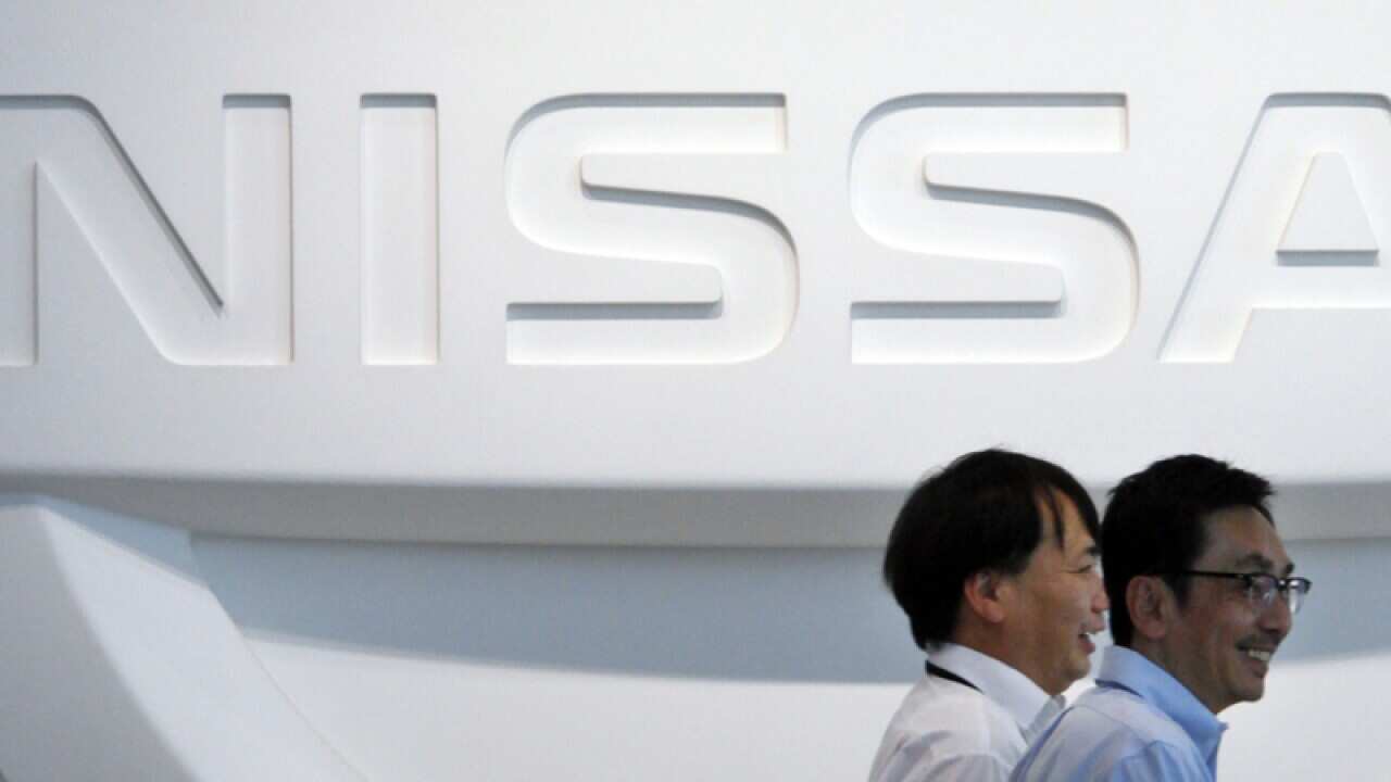 men walk in front of the logo of Nissan Motor Co.