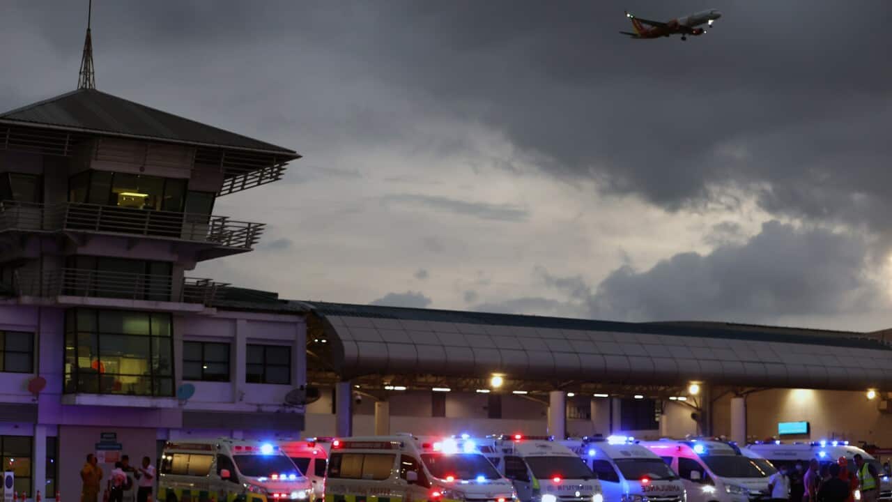 Multiple ambulances with lights on park at the airport, with a plane flying overhead.