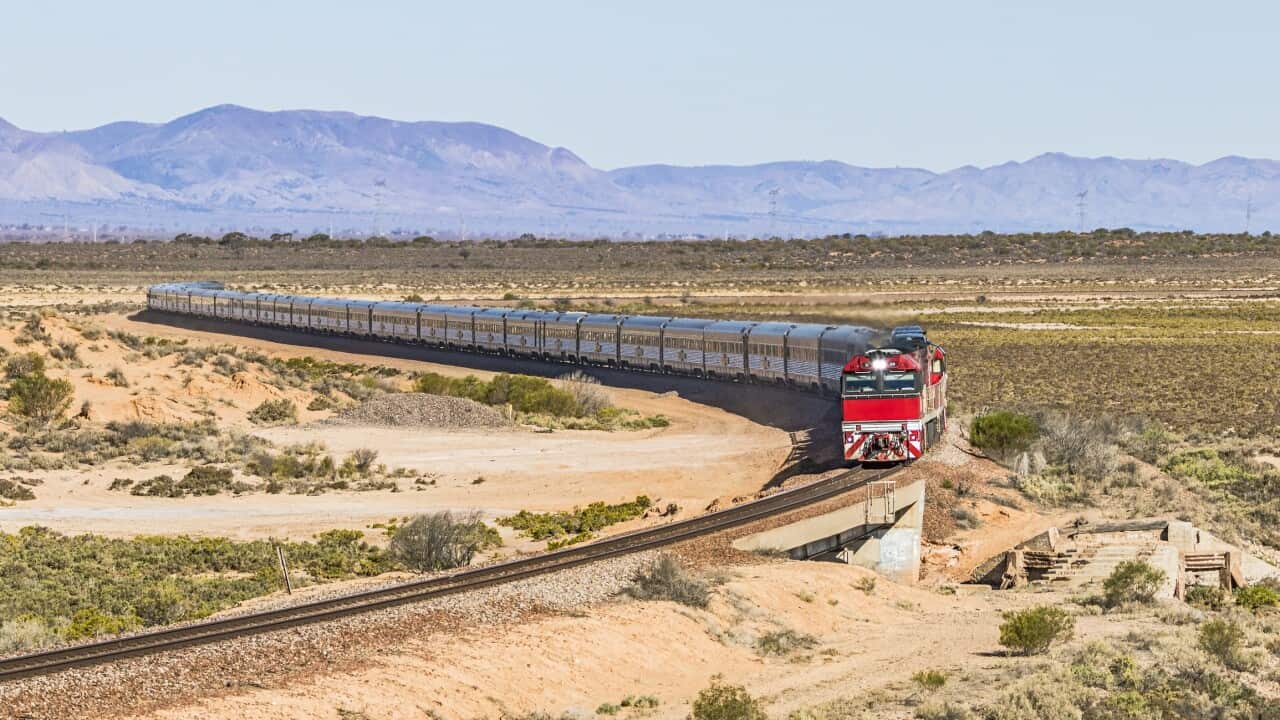 Long distance luxury passenger train with red engine in outback South Australia with Flinders Ranges backdrop