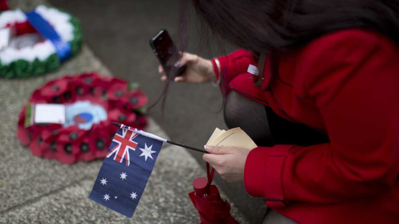 A woman holding an Australian flag takes a picture of wreaths