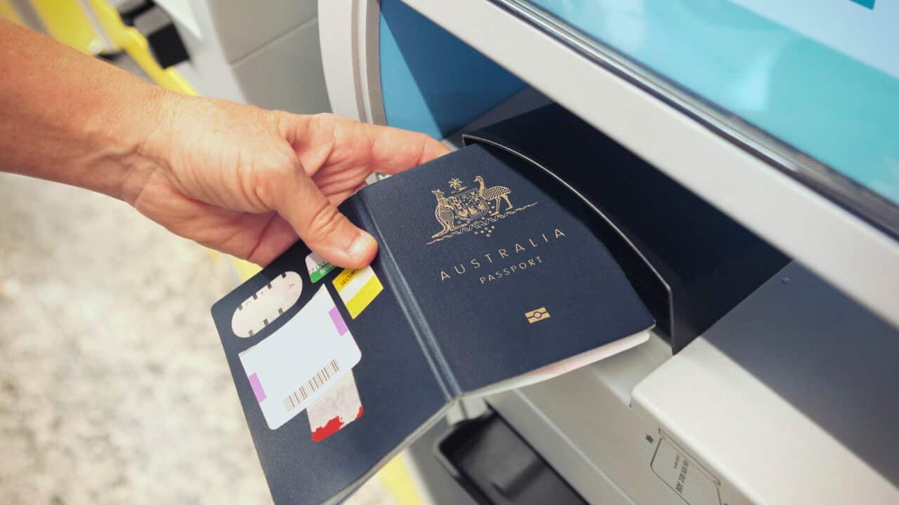 An electronic check-in counter with a person placing an Australian passport to be scanned.
