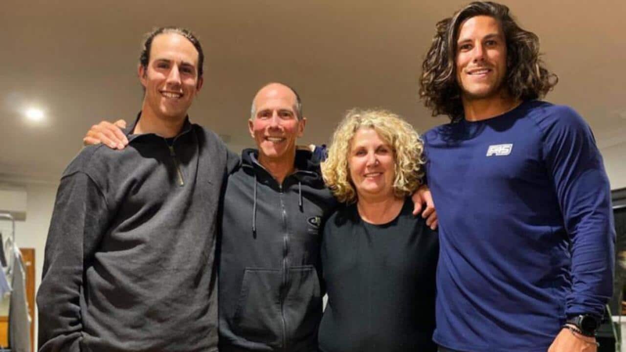 A group of four people posing for a photo with a brown dog at their feet. Two of them are young men with brown hair, one is an older man who is balding, and the fourth is an older woman with blonde hair