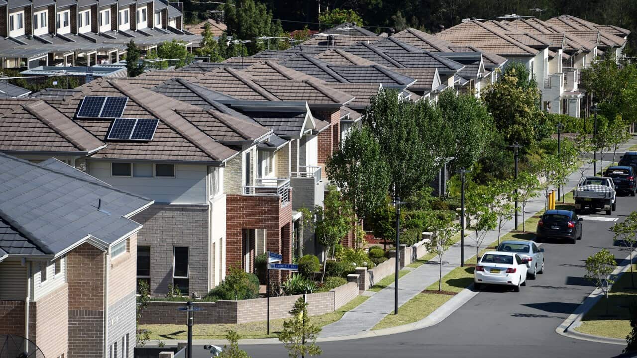 A street view showing a row of houses, with cars parked in the street.