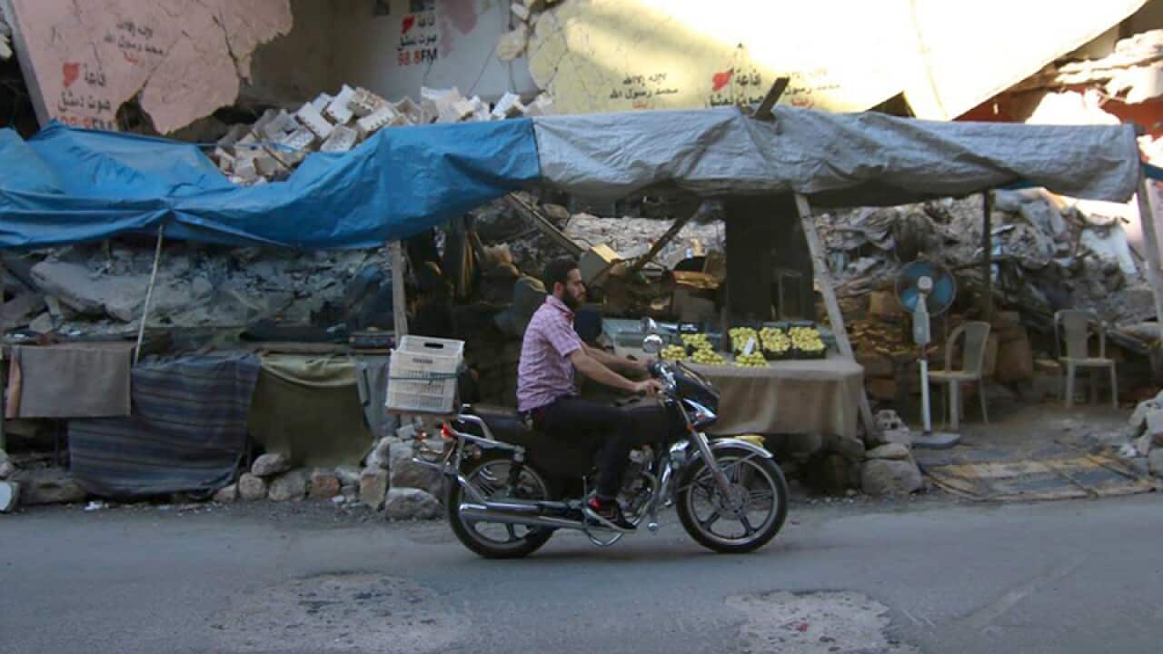 A Syrian man rides a motorcycle past damaged buildings in Aleppo